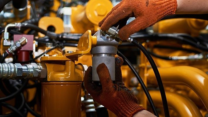Hender i vernehansker justerer en hydraulisk kobling på anleggsutstyr